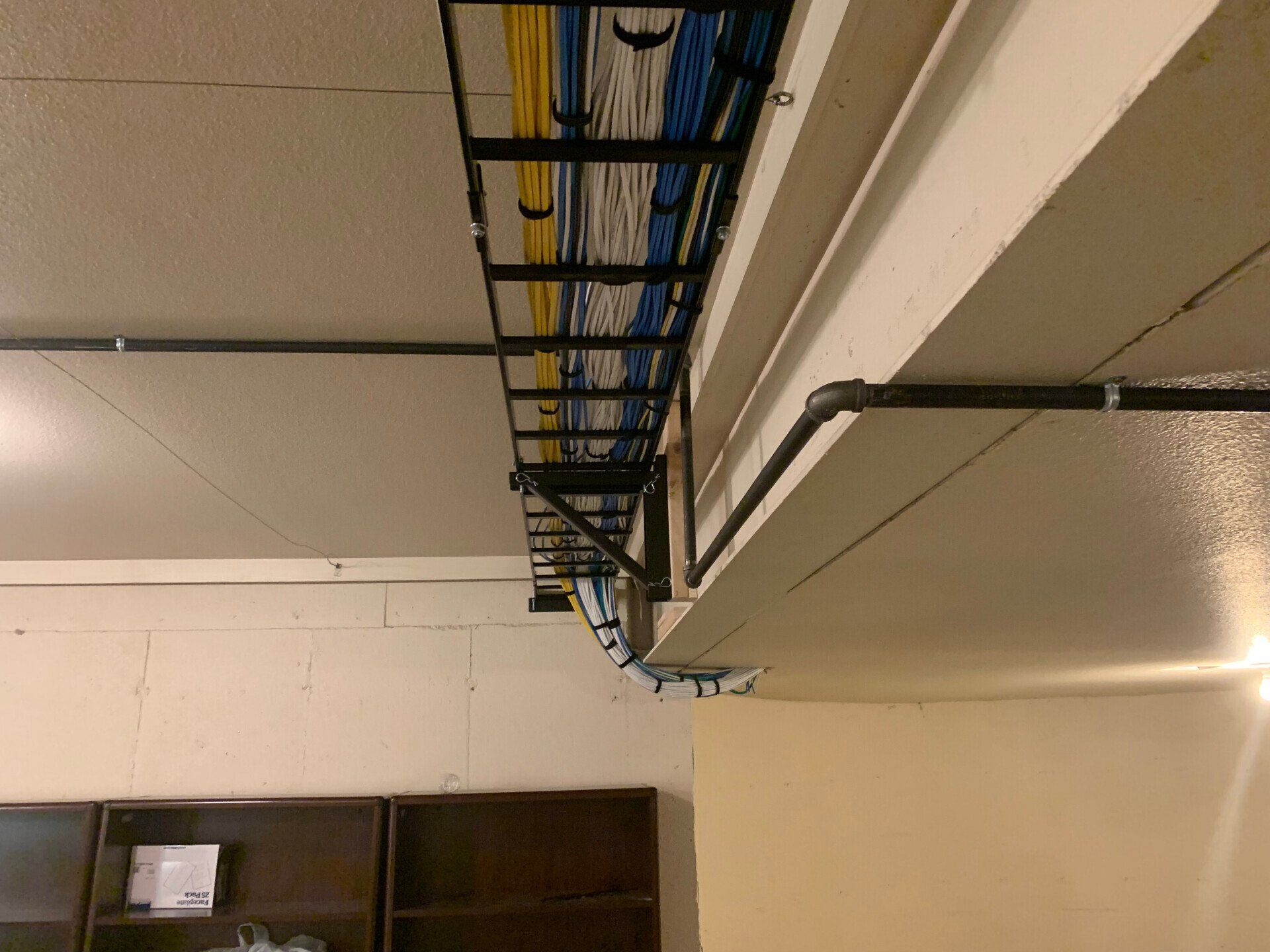 Ceiling cable trays and wiring in a utility room, with a wood cabinet below.
