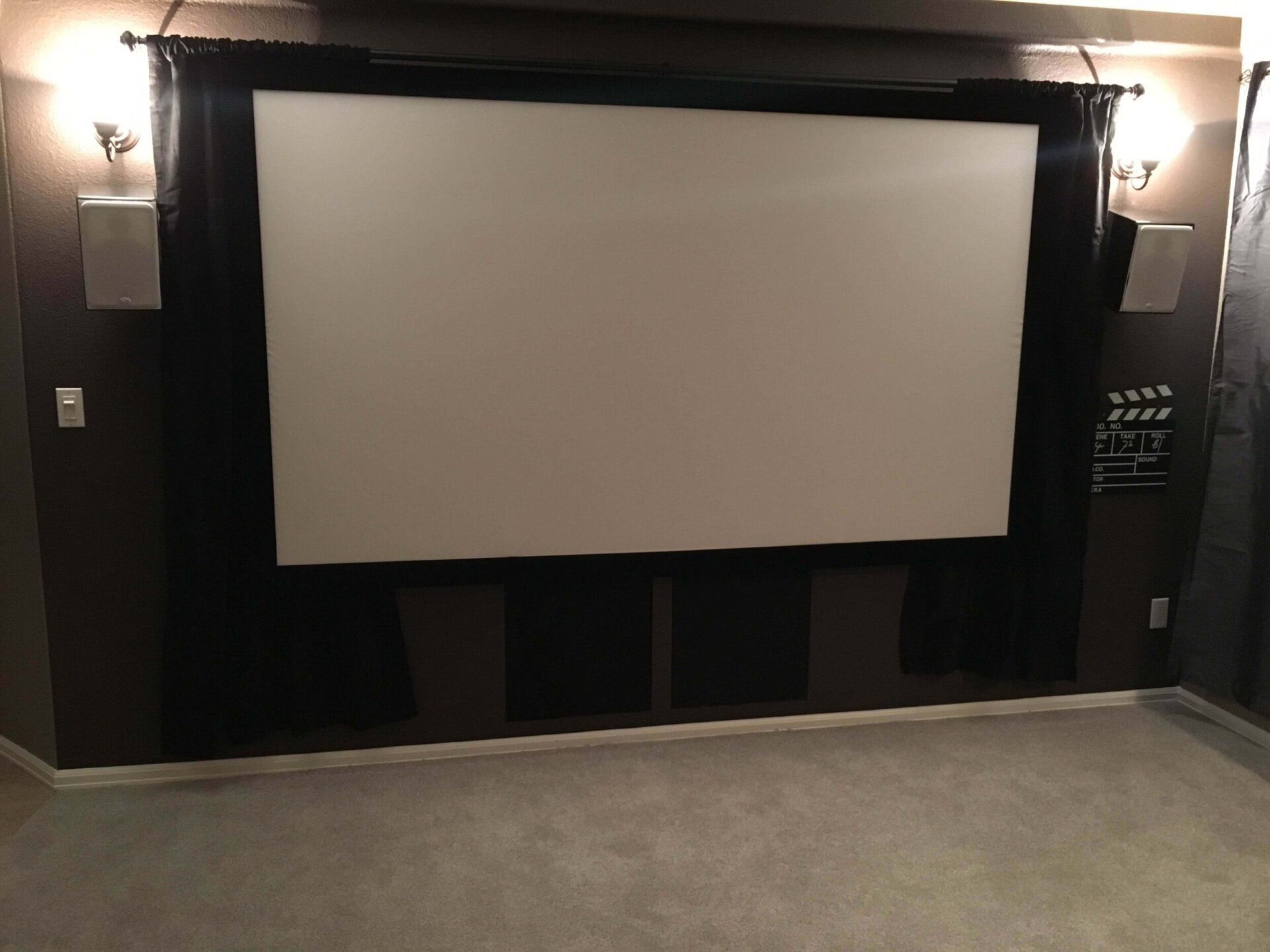 Small home theater with a large white projection screen, dark walls, and wall sconces on either side.