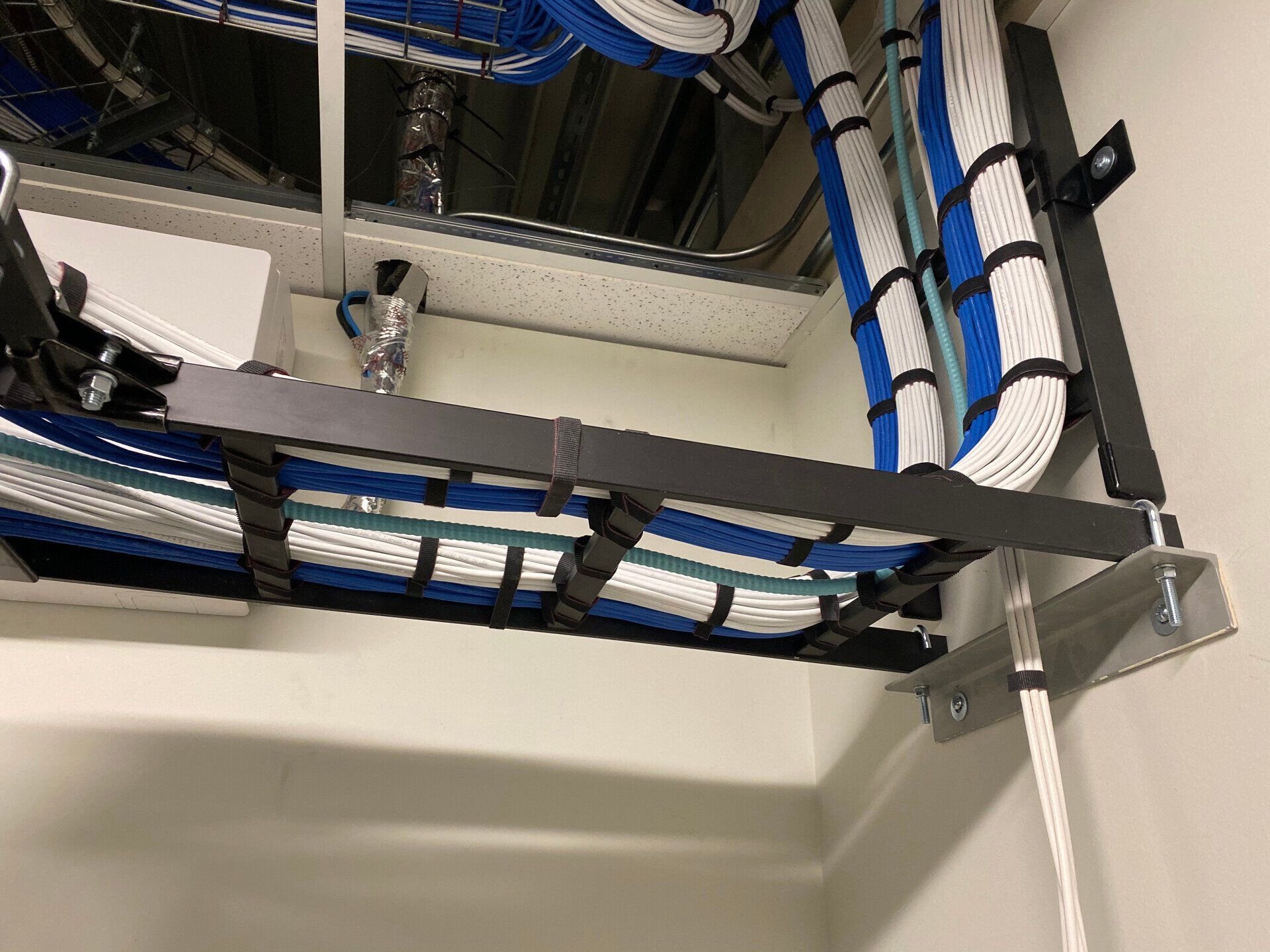 Blue and black cable bundles routed on metal server rack trays in a utility room