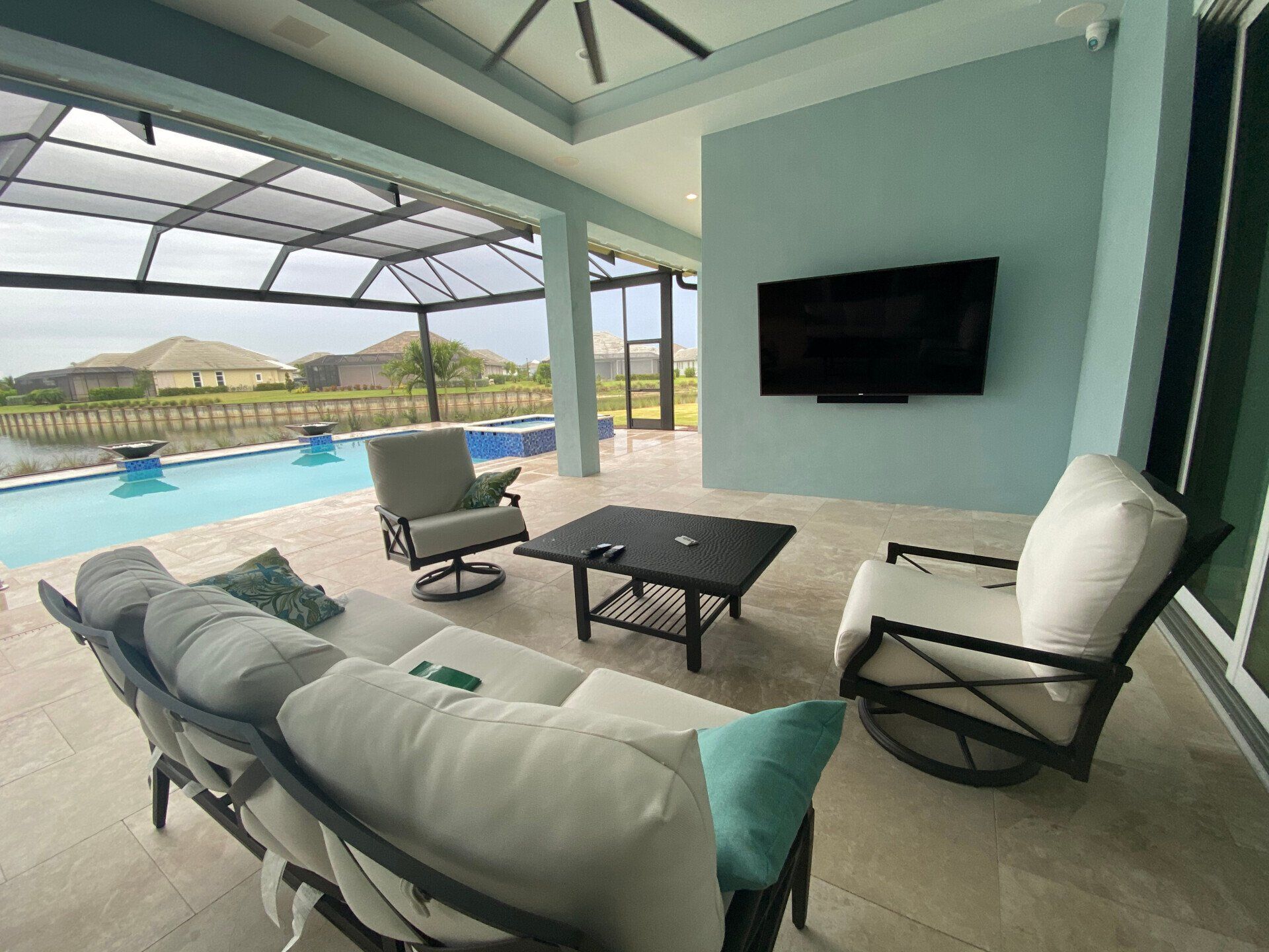 Covered patio with white lounge seating, pool view, and a wall-mounted TV.