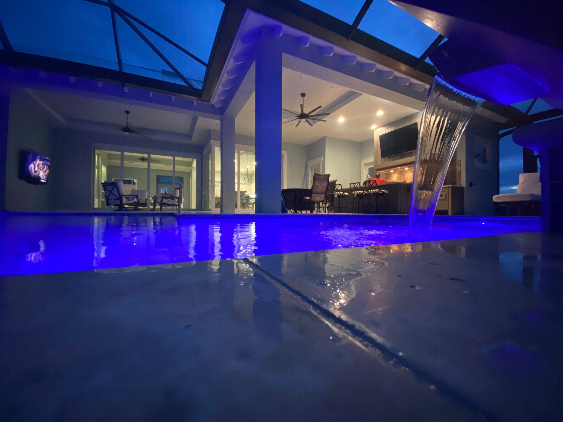 Modern house interior with blue-lit pool in foreground and glass walls at dusk
