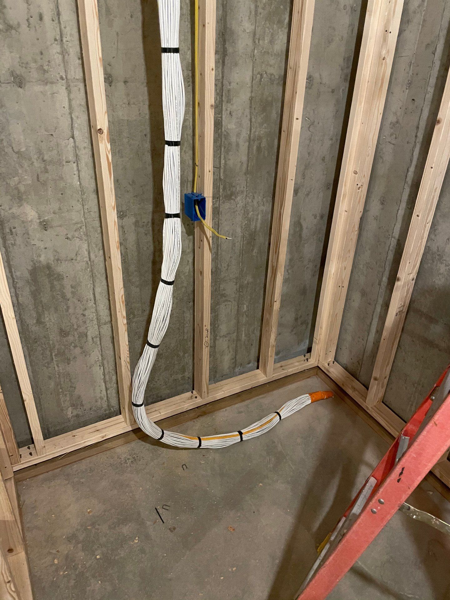 Basement wall framing with insulated ducting, outlet box, and concrete floor near a red ladder