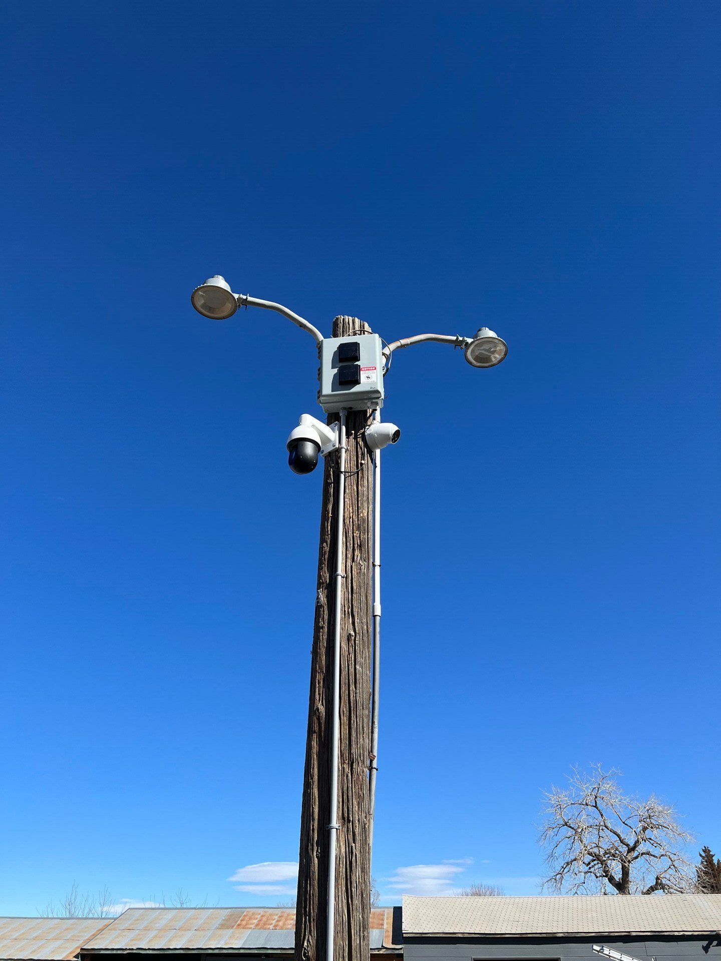 Utility pole with mounted cameras and two lights against a clear blue sky