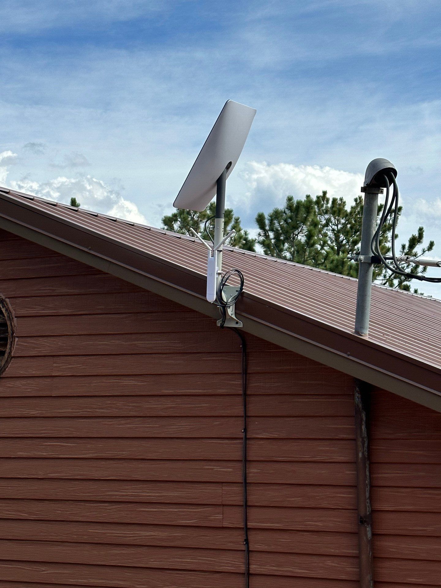 Roof-mounted satellite dish on a red-brown house under a partly cloudy sky