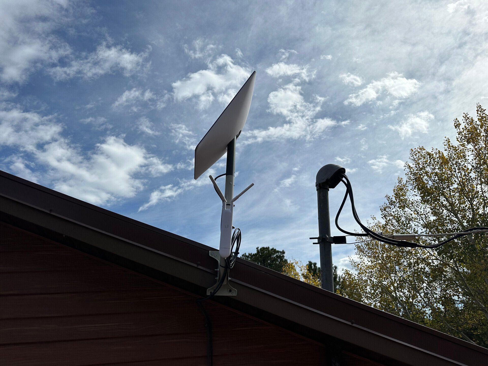 Roof-mounted solar panel and antenna silhouetted against a cloudy blue sky