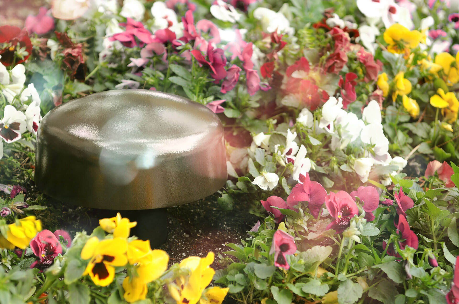 A bronze fountain bowl amid colorful flowers and greenery in a garden pond