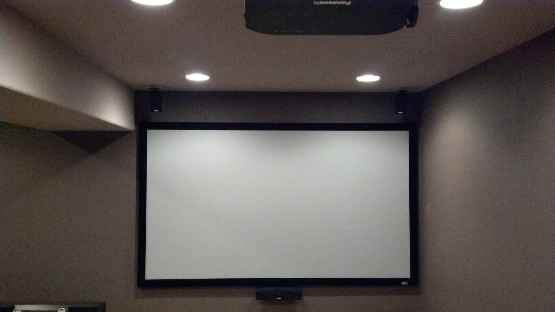 Empty presentation room with a large white projection screen on a dark wall.