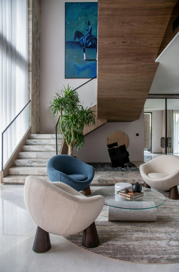 Modern living room with sculptural chairs, round coffee table, staircase, and large blue wall art