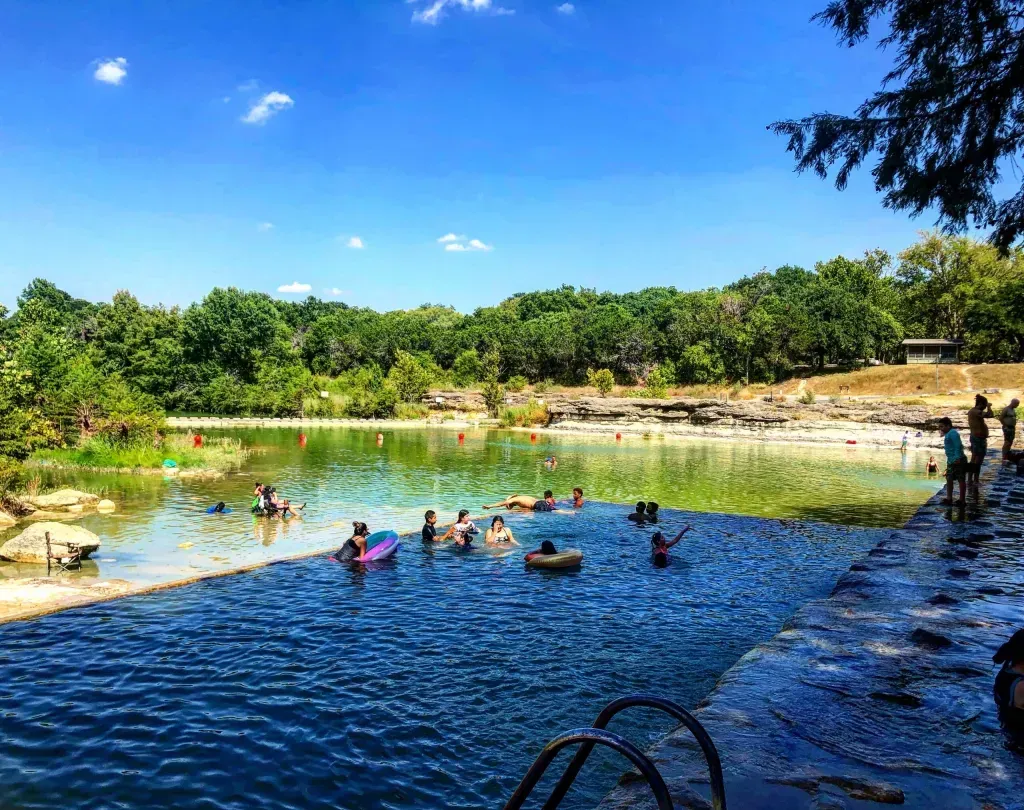 People swimming and relaxing in a blue river pool with green trees and a bright sky
