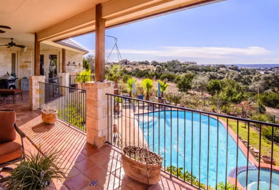 Patio overlooking a sunny backyard with a blue swimming pool and distant hills
