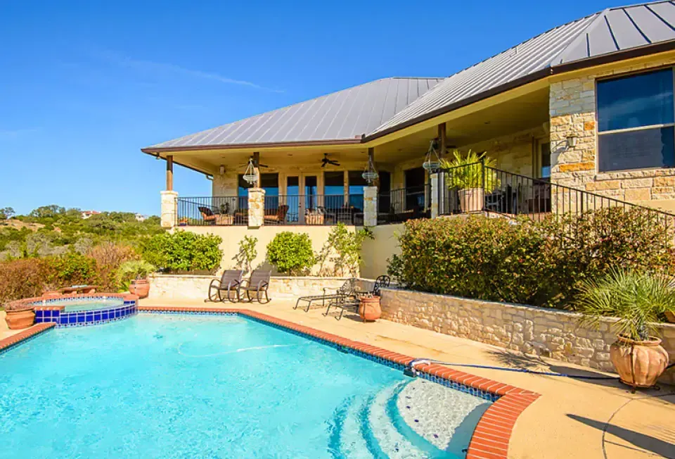 Luxury house with a blue pool, stone patio, and covered veranda in bright sunlight