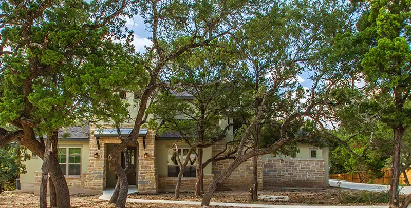 Stone house with a porch under large leafy trees on a sunny day