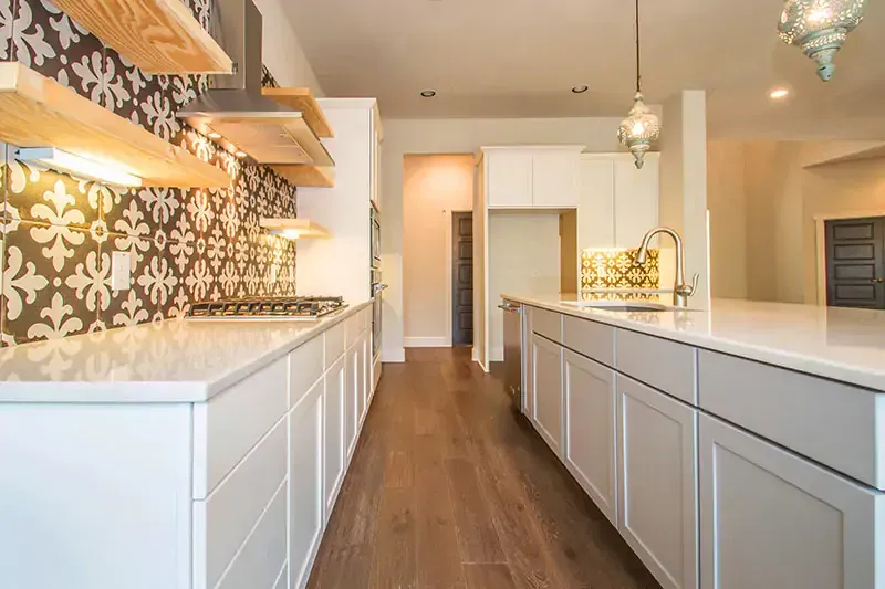 Bright modern kitchen with white cabinets, wood floors, patterned backsplash, and island countertops