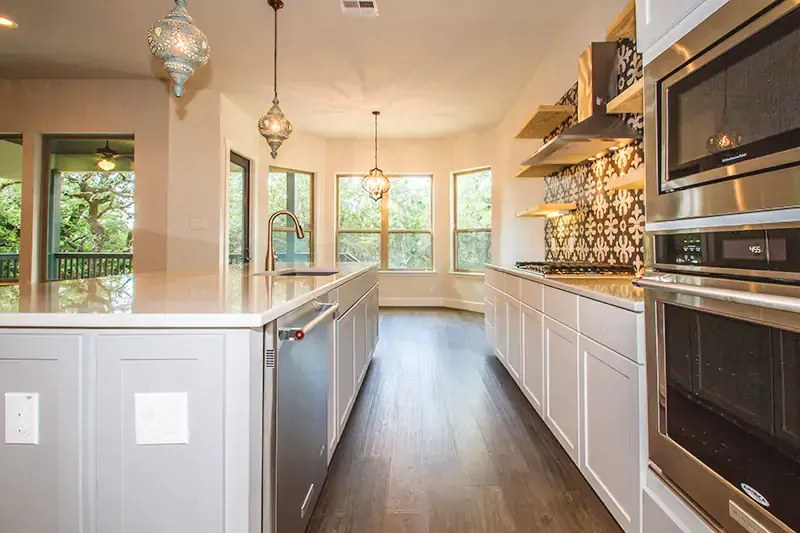 Modern kitchen with white cabinets, dark wood floors, pendant lights, and a large island.