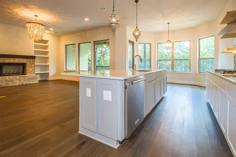 Bright open kitchen with island, hardwood floors, white cabinets, and large windows overlooking greenery