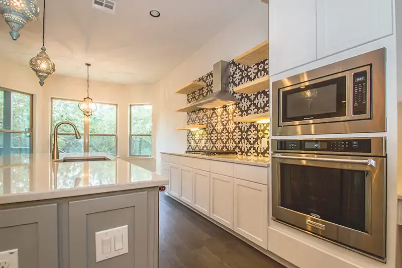 Bright modern kitchen with white cabinets, dark wood floors, pendant lights, and built-in stainless appliances