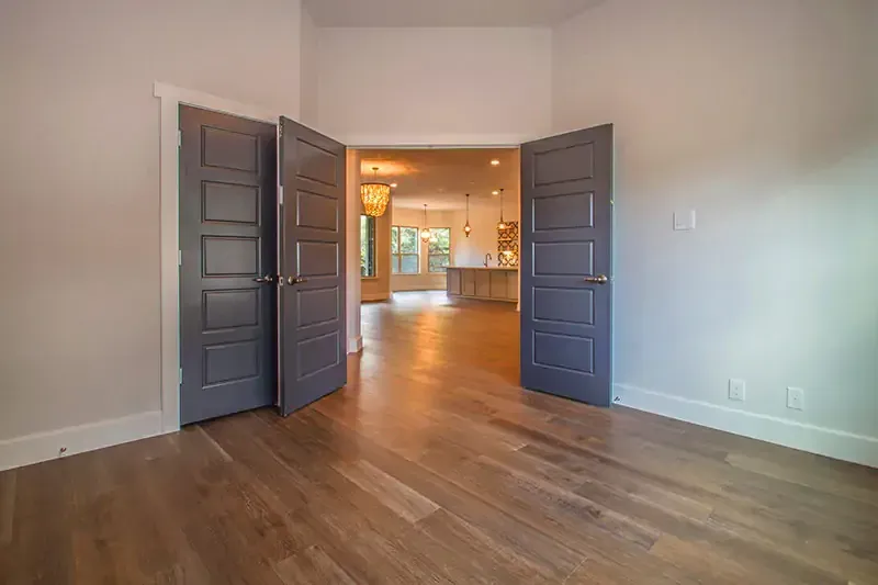 Empty room with dark blue double doors opening to a bright adjoining space and hardwood floors.
