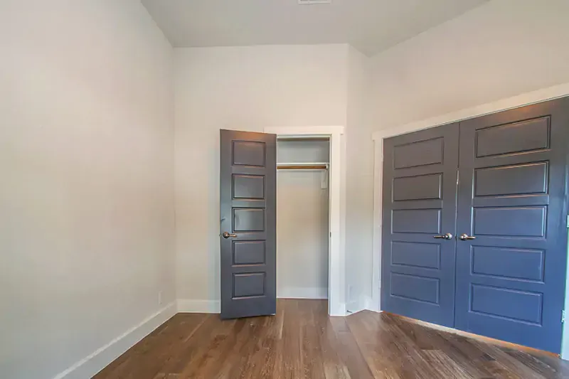 Empty bedroom with blue closet doors, open doorway, white walls, and wood floors