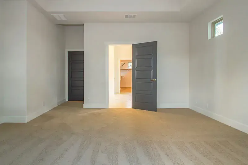 Empty beige room with carpet, open gray door, and bright hallway beyond