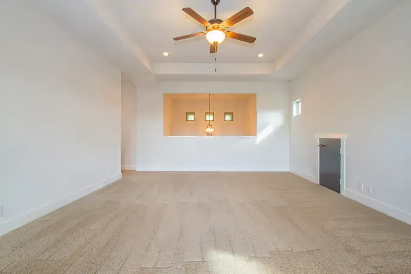Empty living room with beige carpet, white walls, recessed lights, ceiling fan, and a kitchen pass-through window