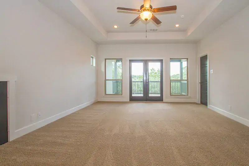Empty beige living room with carpet, ceiling fan, and French doors leading to a balcony.