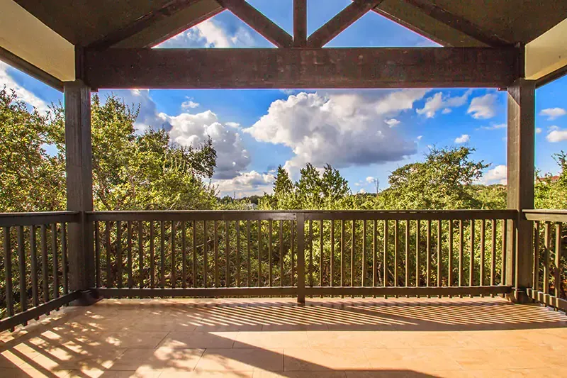 Wooden deck with railing overlooking trees and a blue sky with clouds