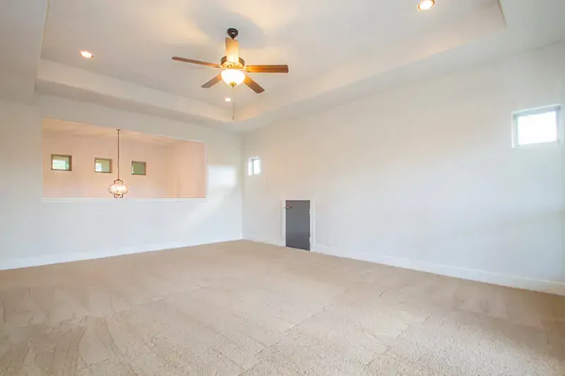 Empty carpeted living room with white walls, ceiling fan, and small windows