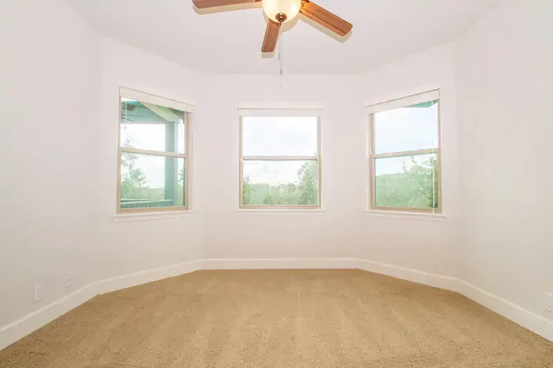 Empty beige bedroom with three windows and a ceiling fan