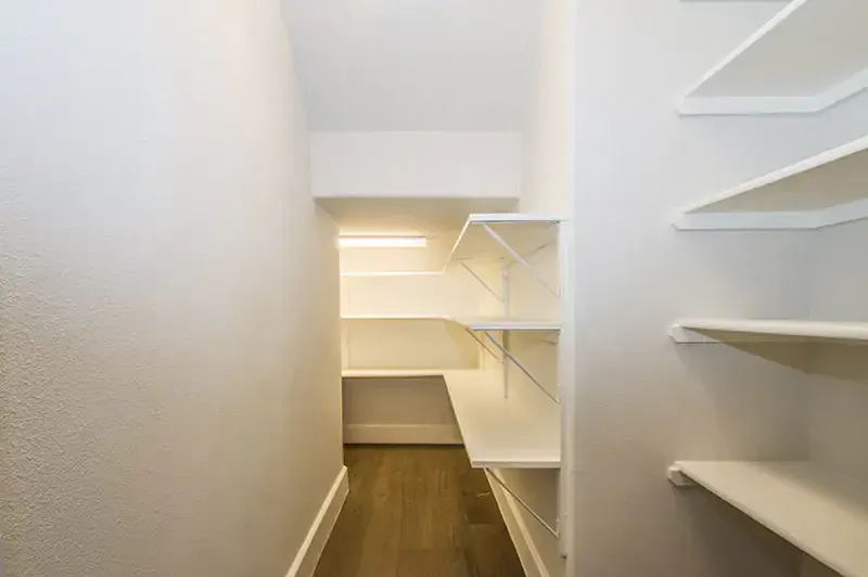Narrow white walk-in closet with built-in shelves and wooden floor