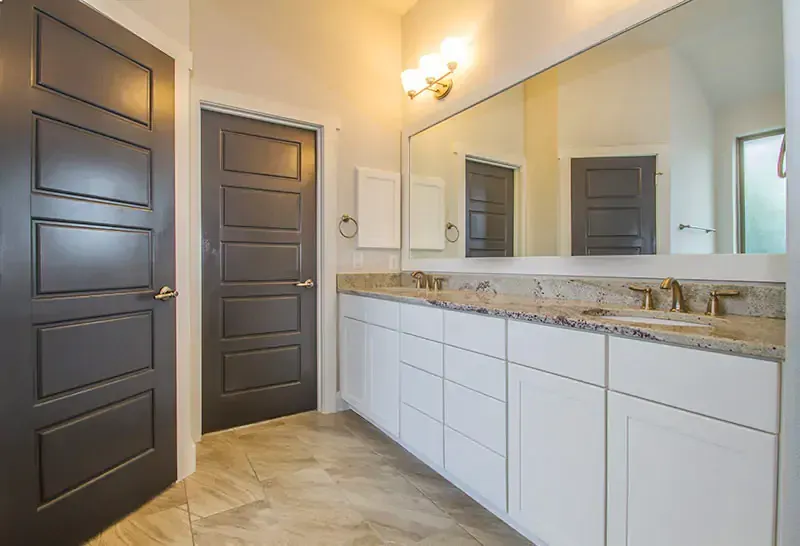 Modern bathroom vanity with white cabinets, granite countertop, large mirror, and gray doors.