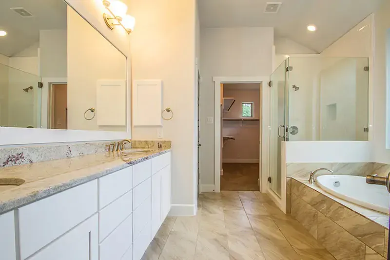 Bright bathroom with double vanity, large mirrors, glass shower, and built-in bathtub.