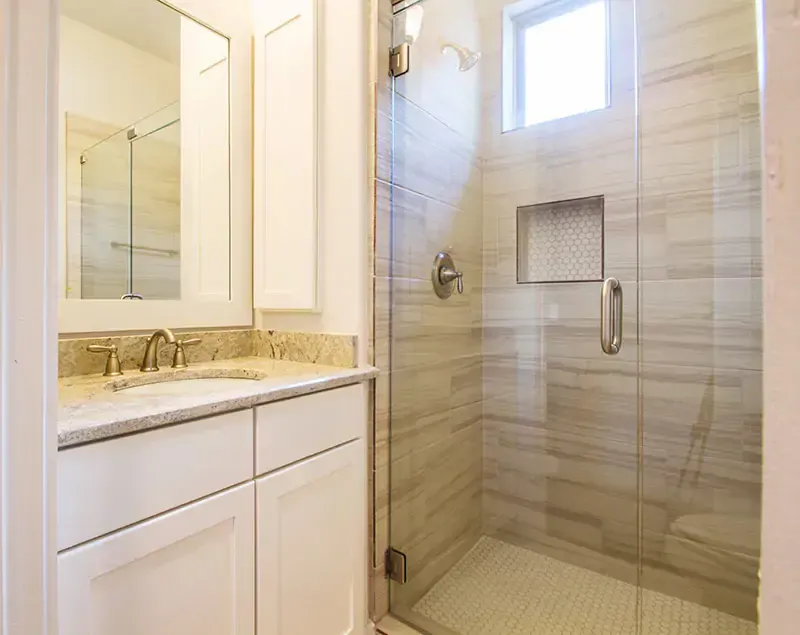 Modern bathroom with white vanity, granite countertop, mirror, and glass-enclosed shower with beige tile.