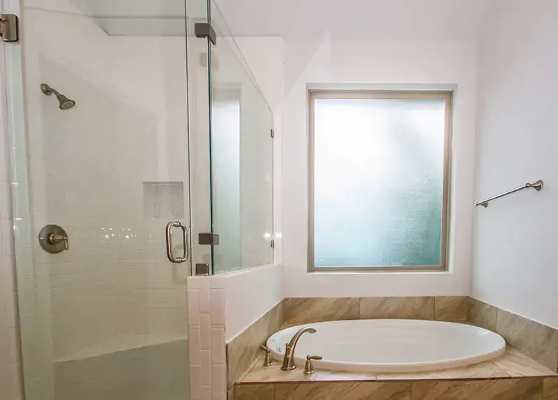 Bright bathroom with a glass shower, frosted window, and built-in soaking tub.