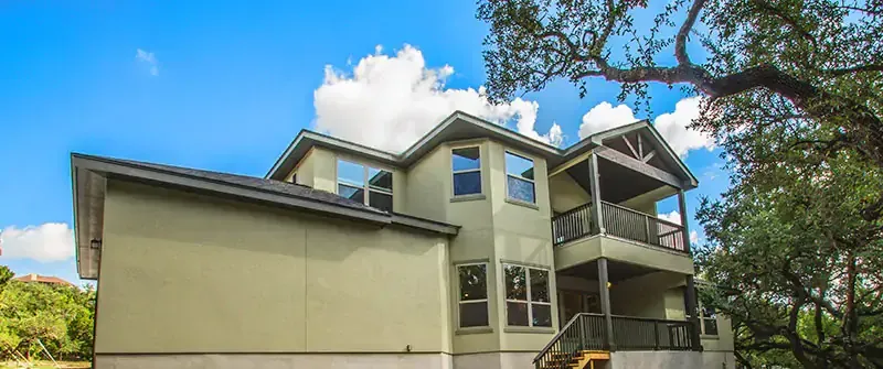 Two-story beige house with a covered porch and balcony under a blue sky.