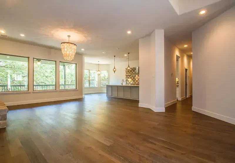 Spacious empty living room with hardwood floors, large windows, and a chandelier.