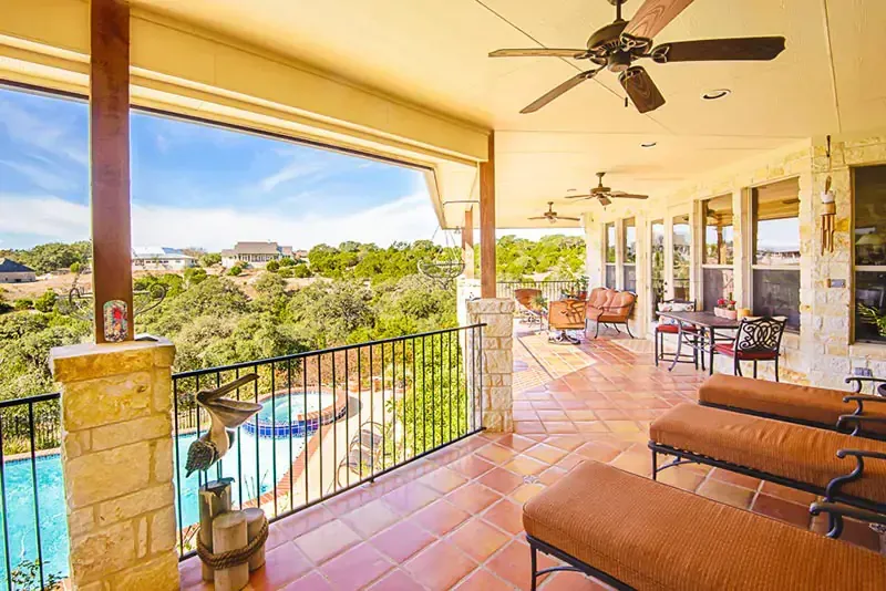 Covered patio with wicker seating, ceiling fan, and views of a pool and green landscape