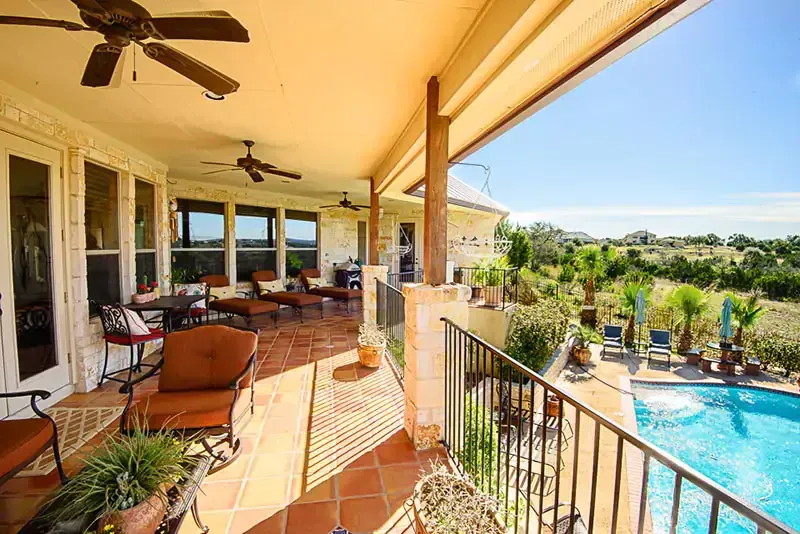 Covered patio overlooking a blue swimming pool and landscaped backyard on a sunny day