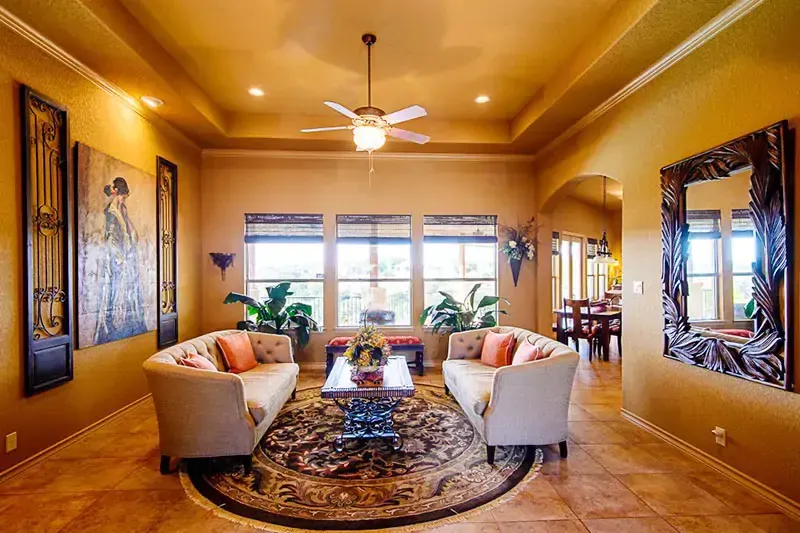 Elegant living room with cream sofas, patterned rug, ceiling fan, and bright windows at the back
