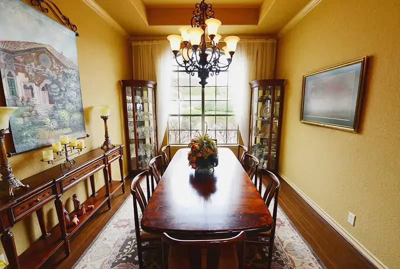Elegant dining room with long wooden table, chandelier, yellow walls, and china cabinets by a window