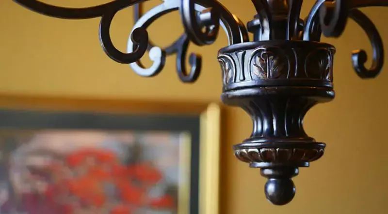 Close-up of an ornate black chandelier against a blurred warm-toned background