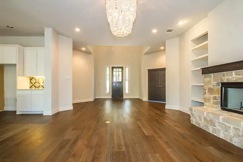Bright empty living room with hardwood floors, white walls, stone fireplace, and built-in shelves