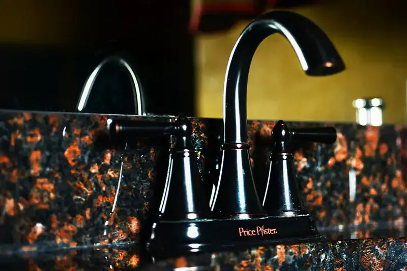 Black and copper kitchen faucet on a granite countertop with warm reflections