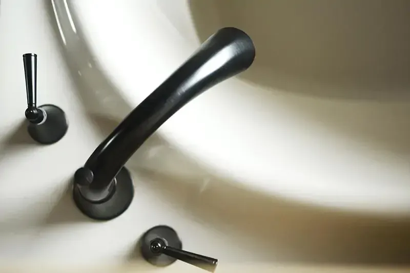 Three black bathroom faucet handles on a white sink countertop