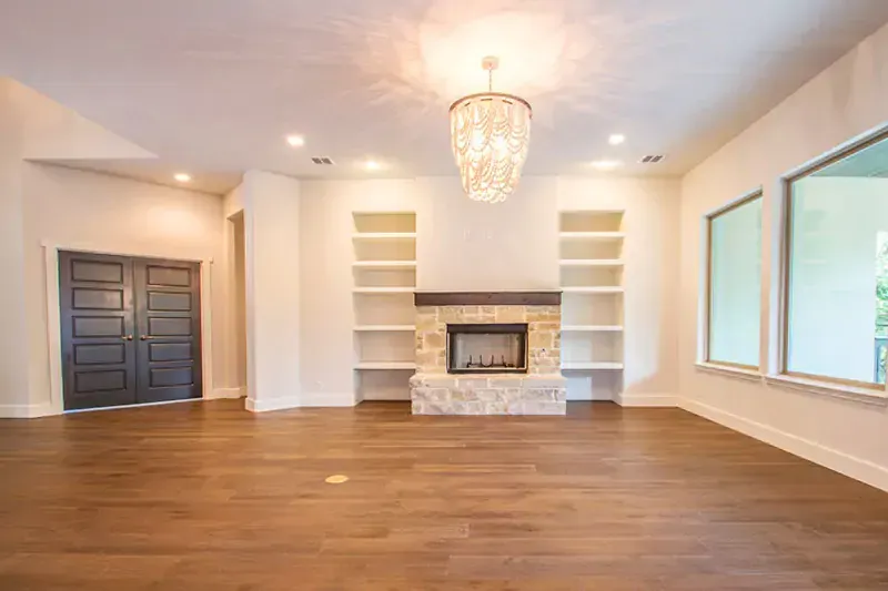 Bright empty living room with hardwood floors, stone fireplace, built-in shelves, and large windows