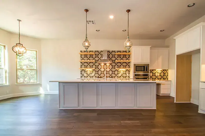 Bright open kitchen with white cabinets, gray island, pendant lights, and patterned backsplash