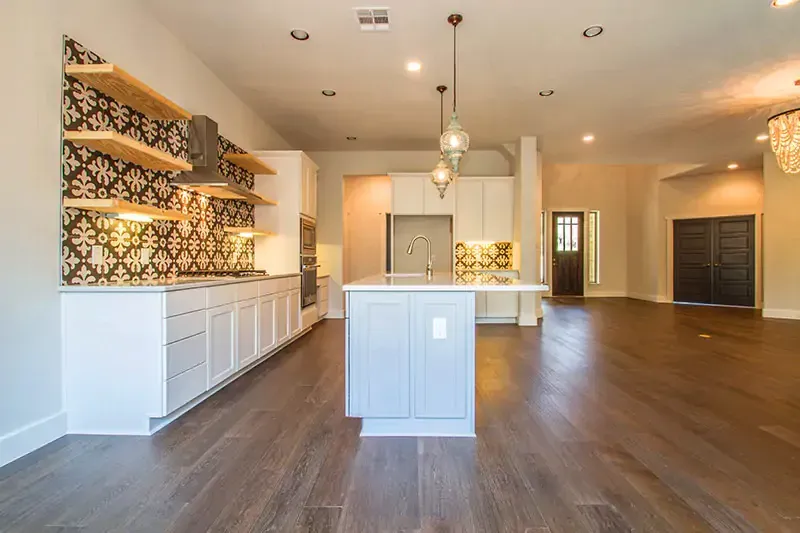 Spacious modern kitchen and living area with white cabinets, wood floors, and patterned backsplash shelves