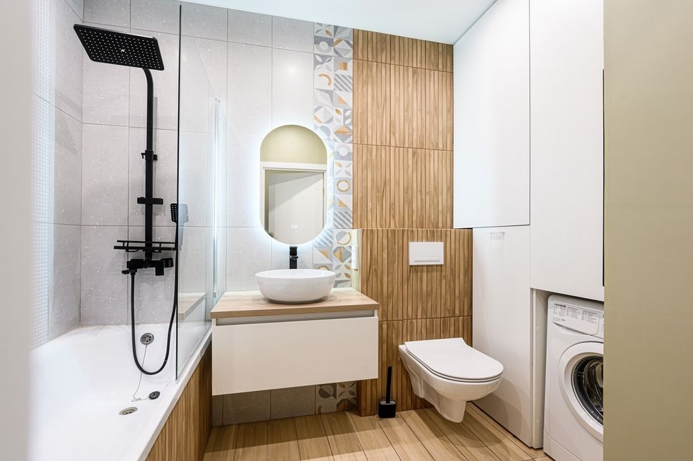 Modern bathroom with white, wood, and patterned tile accents. Includes shower, sink, toilet, and washing machine.