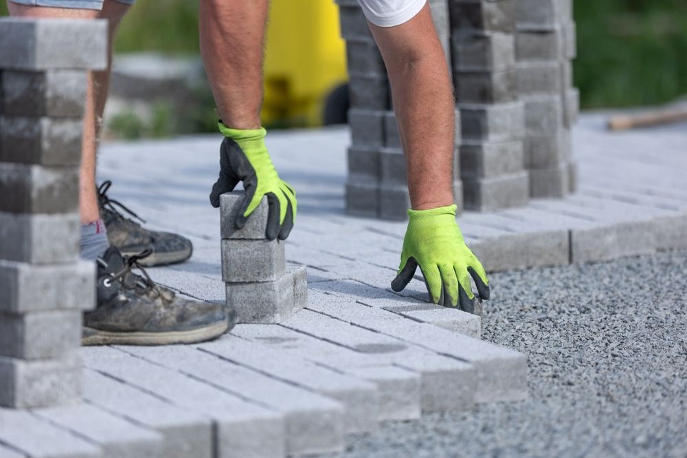 Person wearing neon green work gloves laying paving stones.