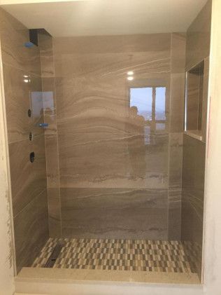 Tiled shower with beige walls, patterned floor, and a small window.