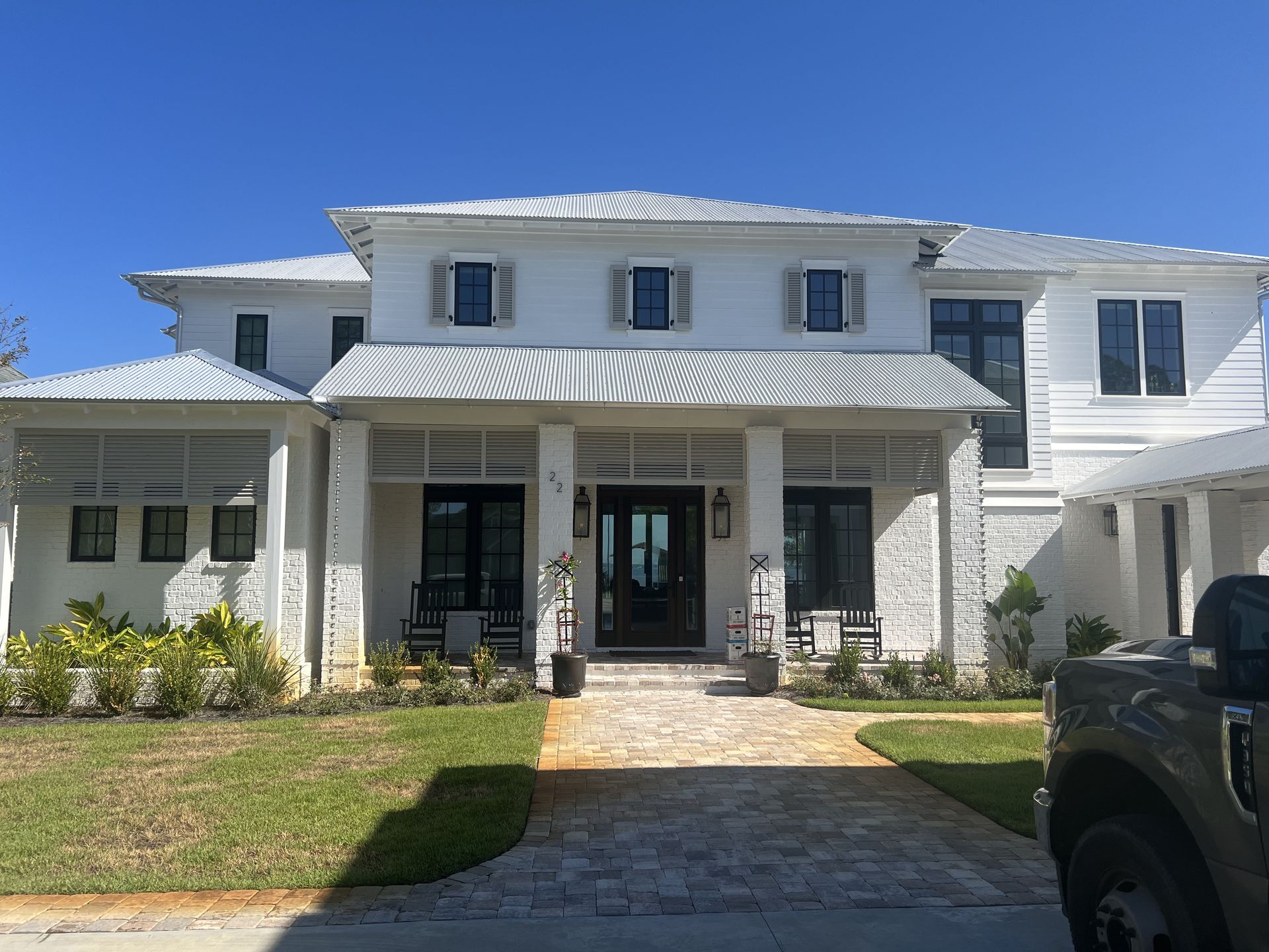 White house with gray roof, black window frames, shutters, and doors; porch with seating.